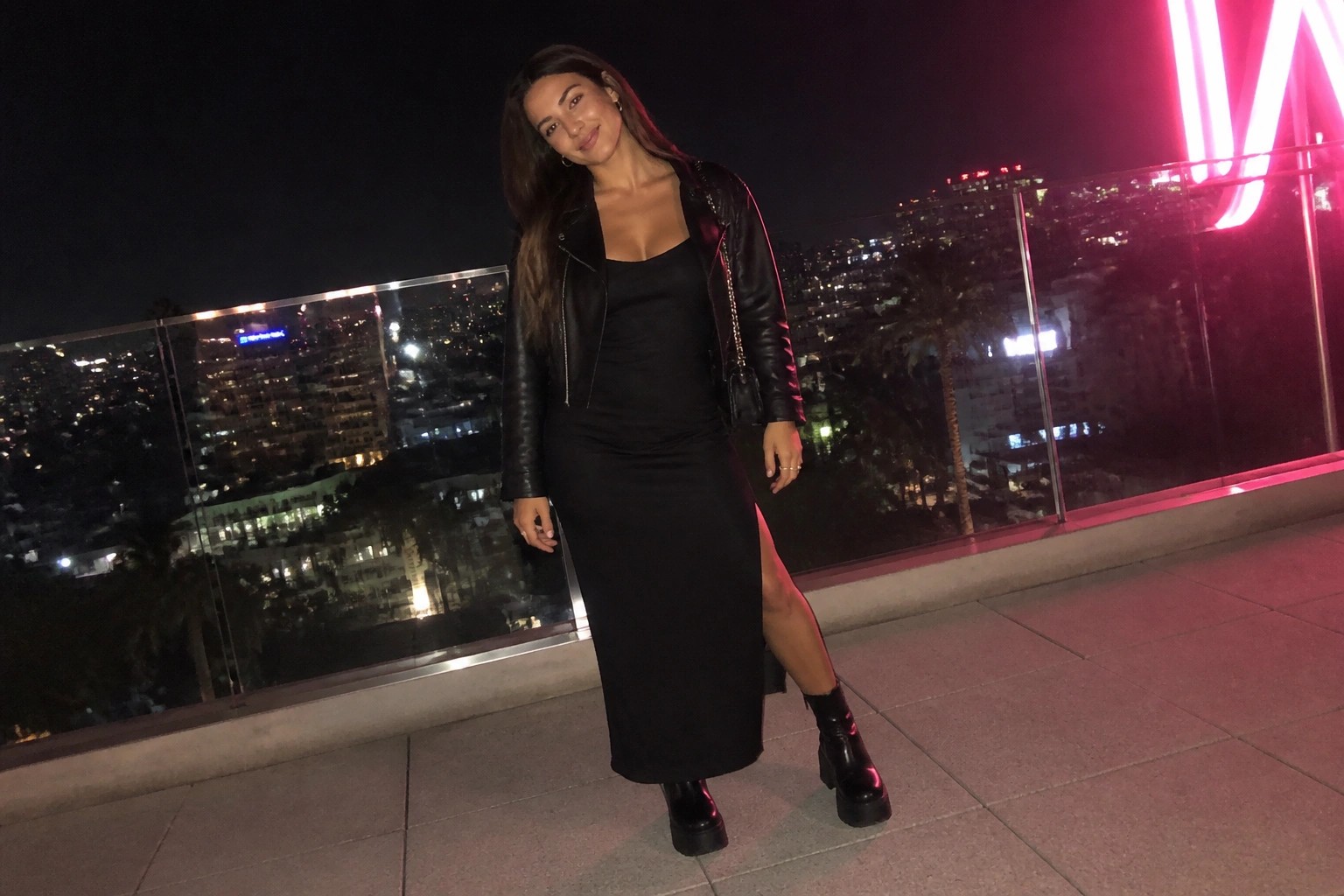 Woman in black satin dress and leather jacket on NYC rooftop at night with I Love NY sign
