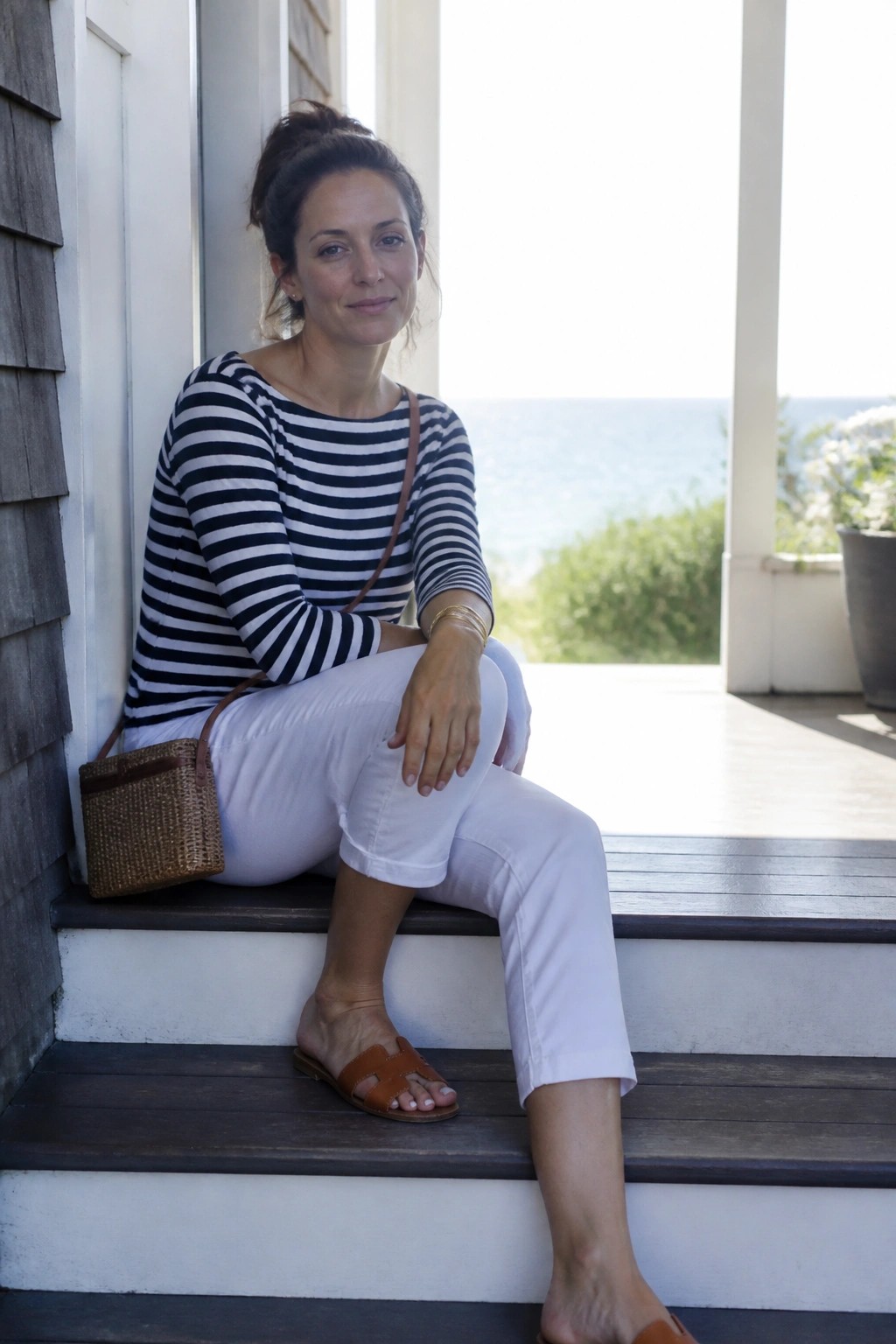 Woman in striped shirt and white pants on porch steps with ocean view
