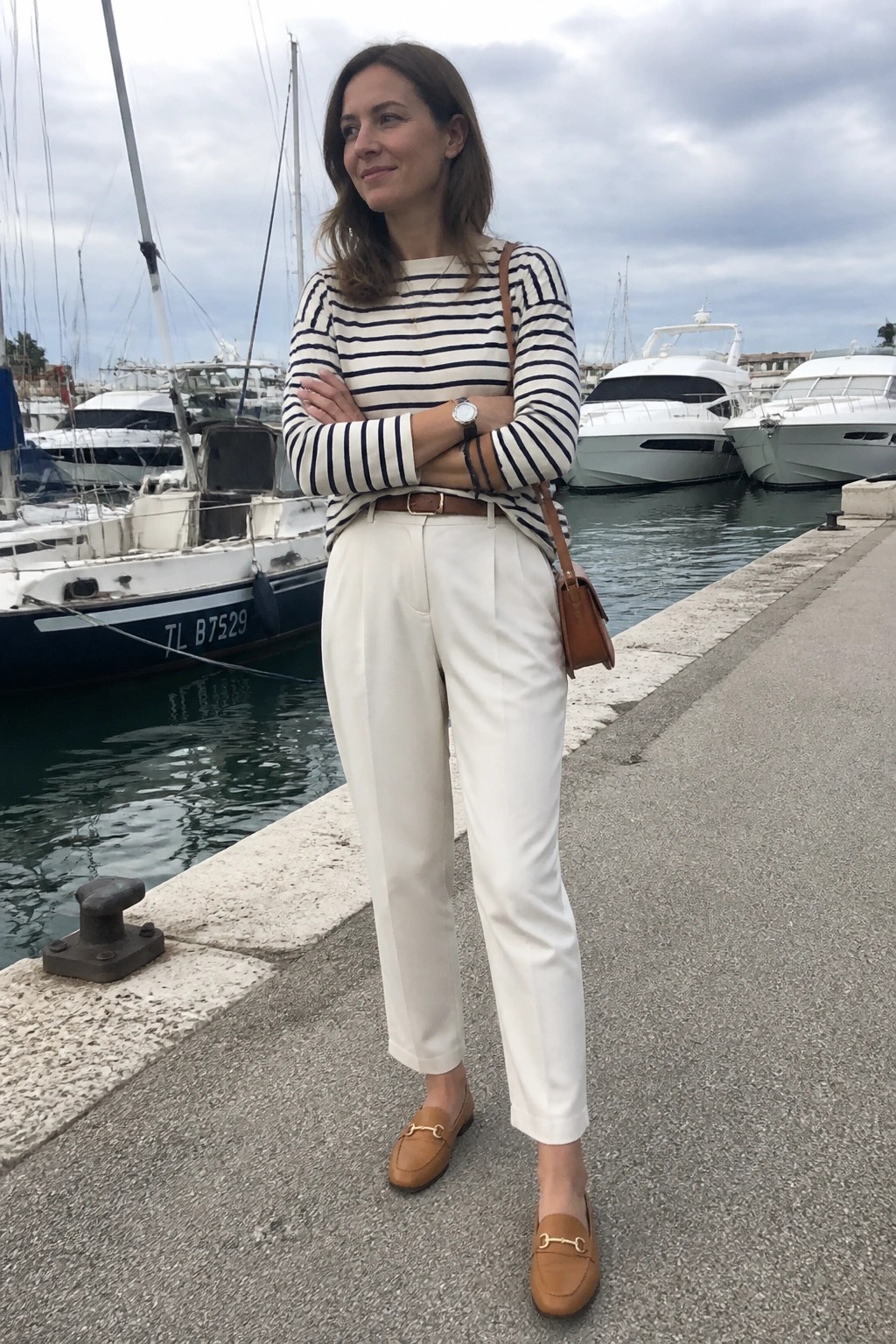 Woman with arms crossed in striped top and white pants at marina.