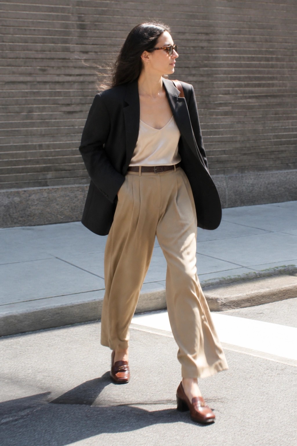 Woman in black blazer, beige camisole and wide-leg trousers on sunny street.