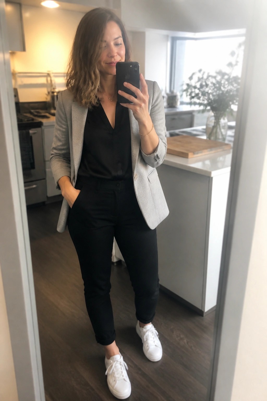 Woman in gray blazer and black pants taking mirror selfie in kitchen
