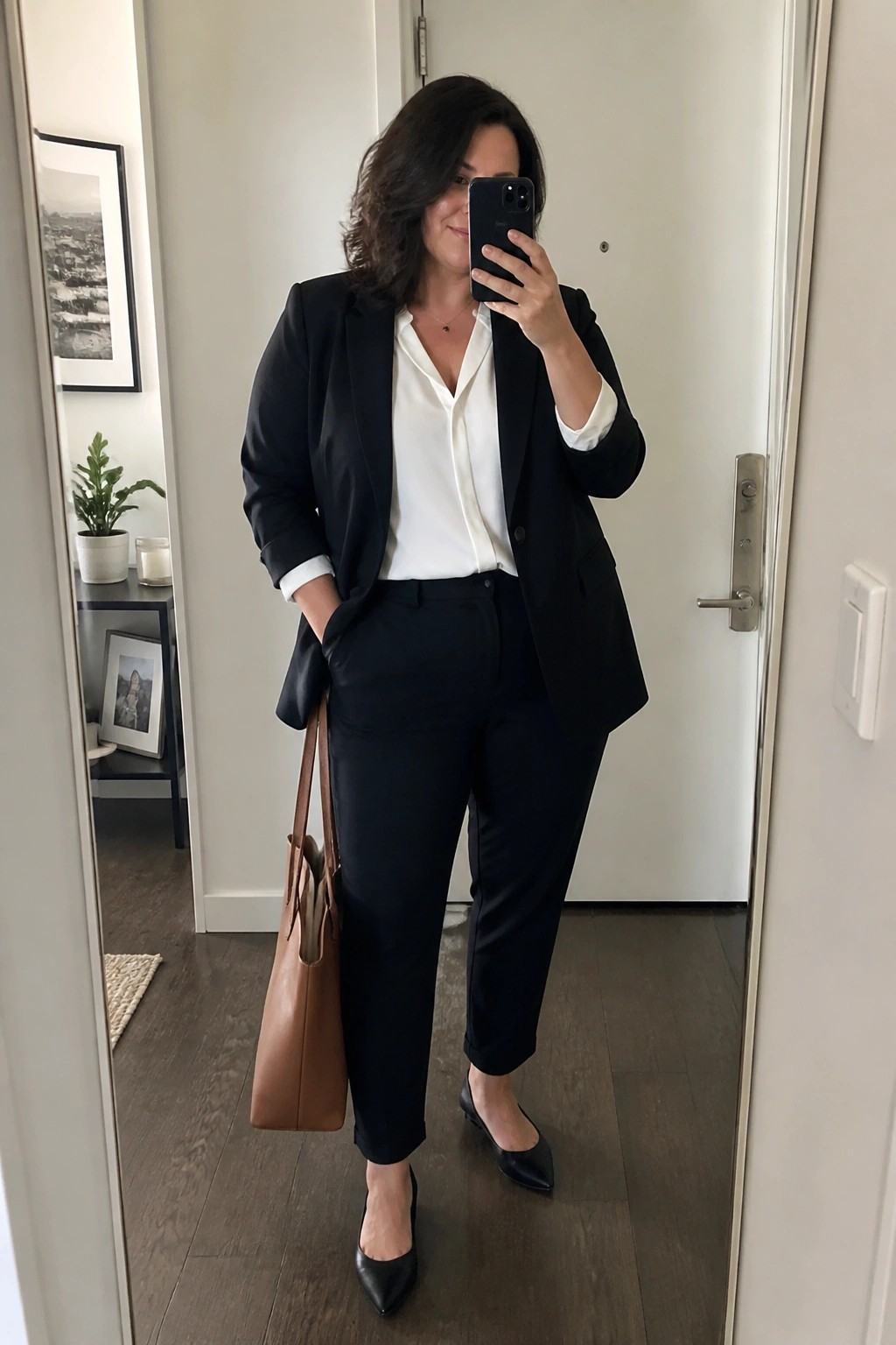 Woman in black blazer and pants taking mirror selfie with brown handbag