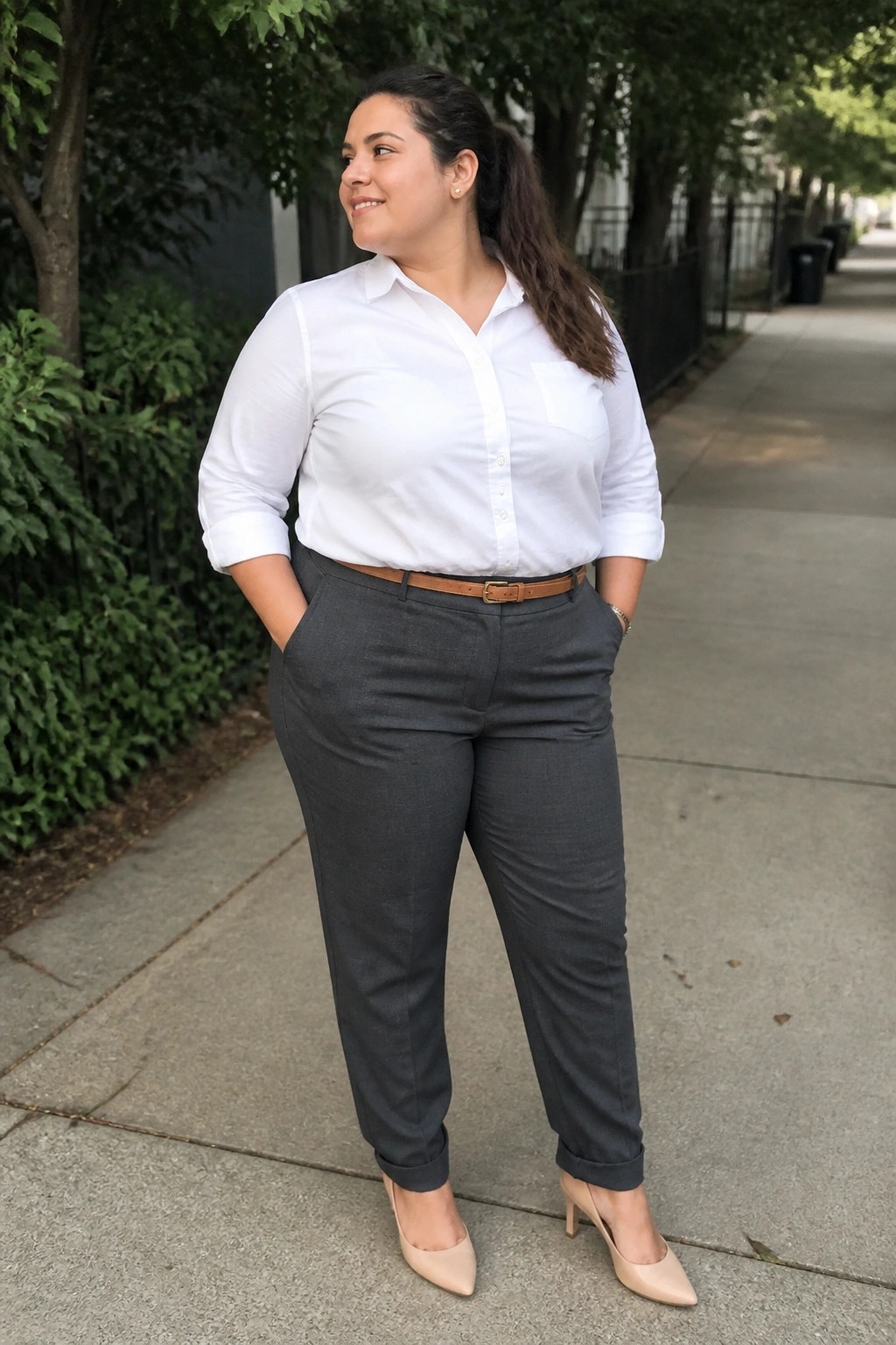 Woman in white shirt and gray pants with hands in pockets on sidewalk