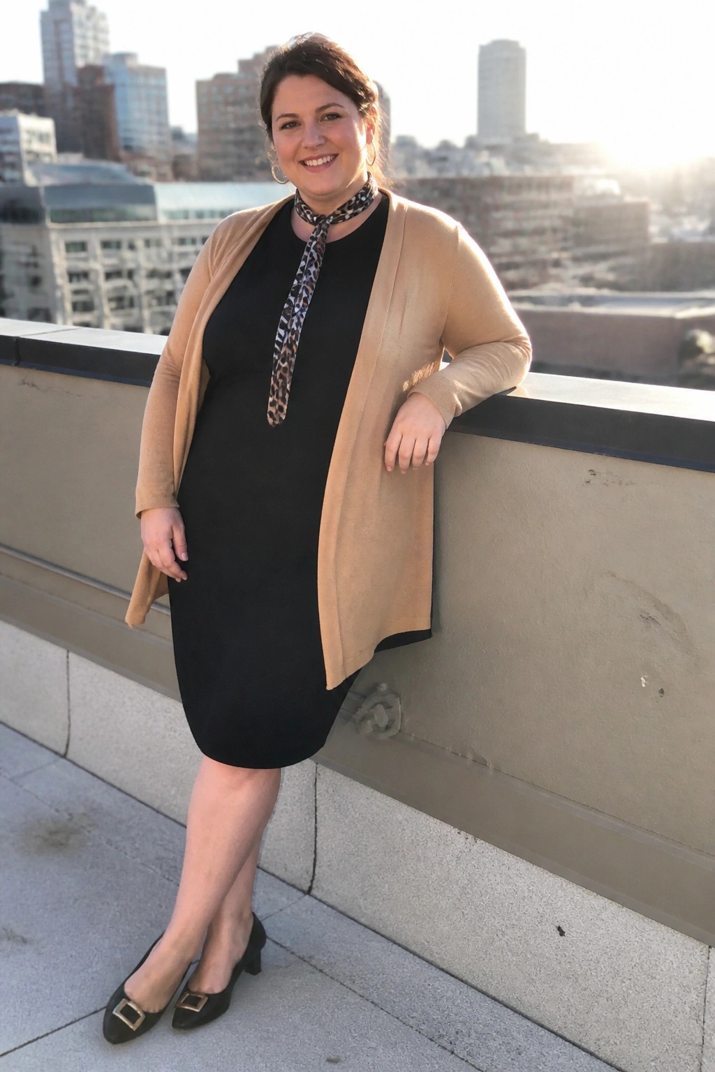 Woman in black dress, beige cardigan, and leopard scarf on city balcony