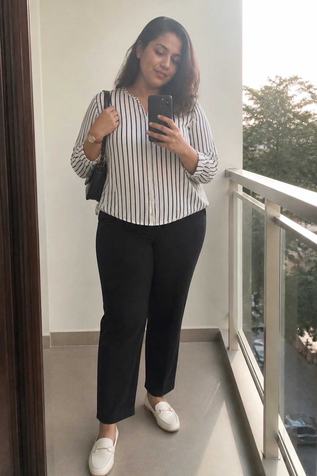 Woman in striped blouse and black pants taking selfie on balcony
