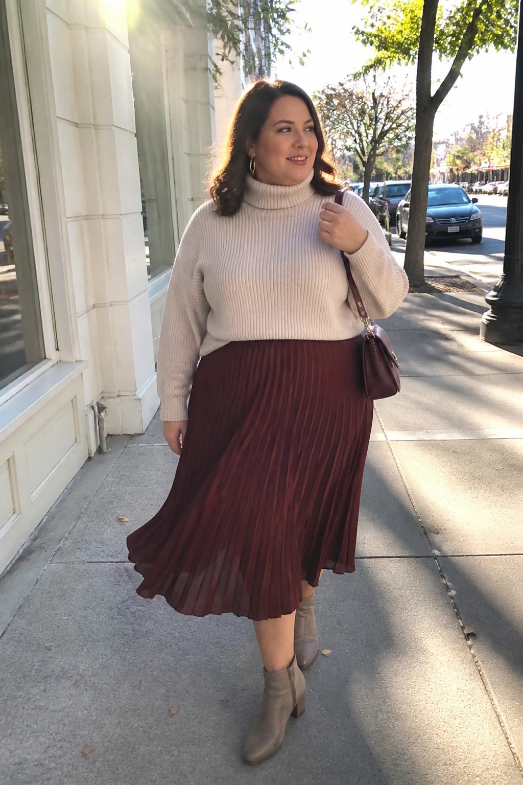 Woman in cream turtleneck and burgundy pleated skirt on sunny sidewalk