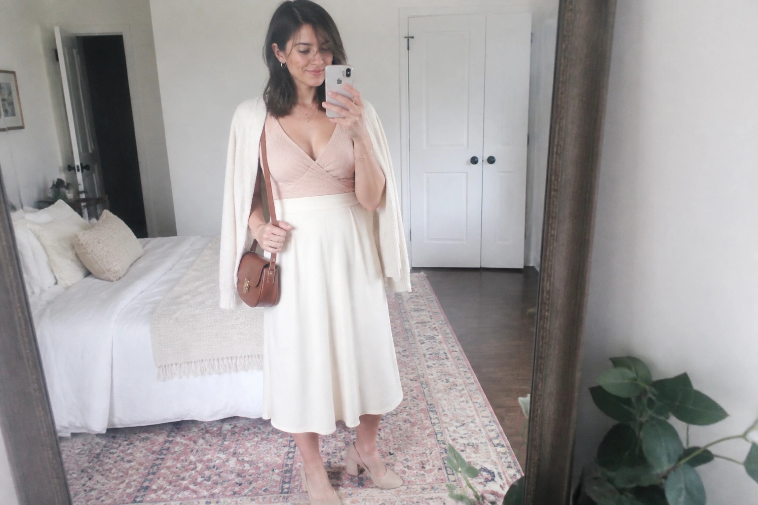 Woman in pink top and cream cardigan taking bedroom mirror selfie