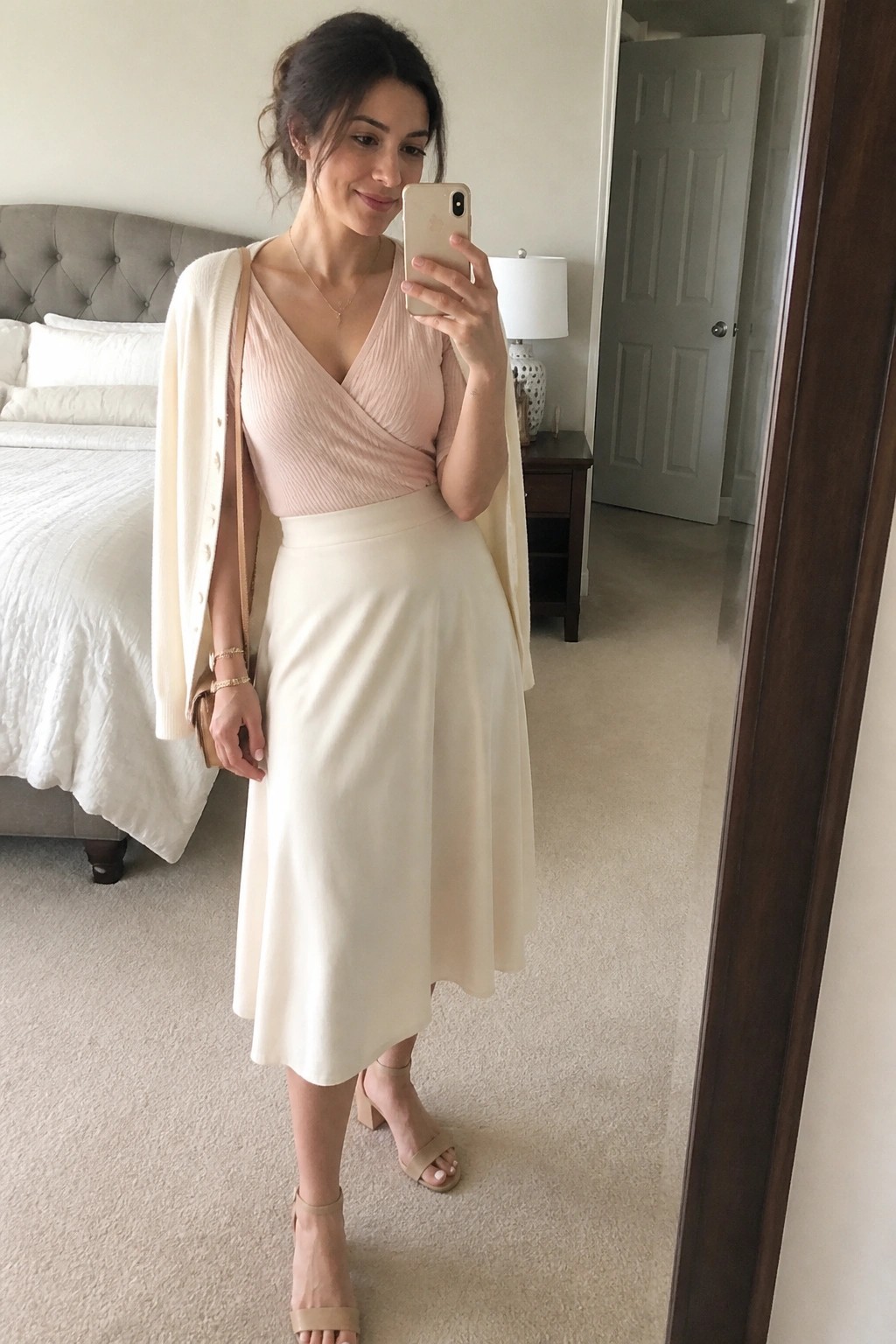 Woman in pink top and cream cardigan taking bedroom mirror selfie