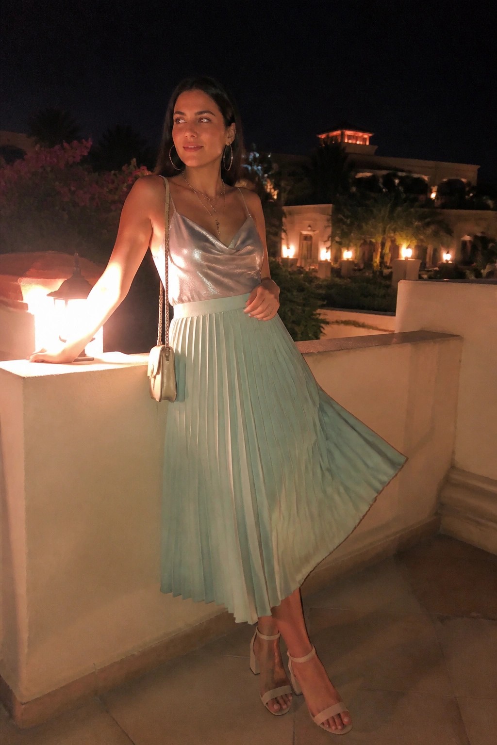 Woman in metallic silver top and mint green pleated skirt on night balcony