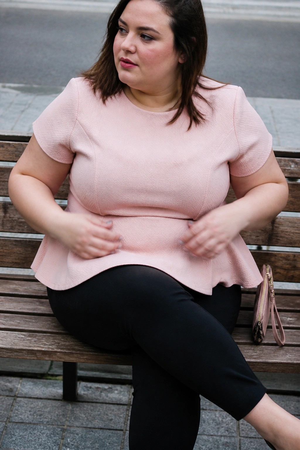 Woman in pink peplum top and black pants seated on wooden bench with wallet