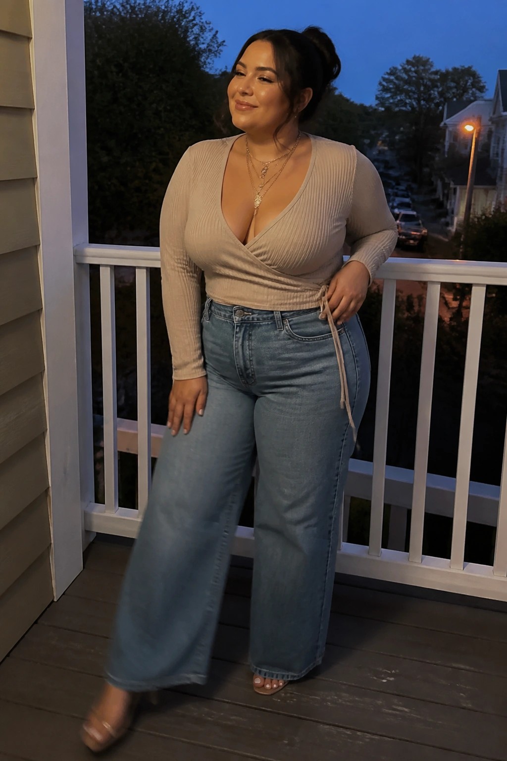 Woman in beige wrap top and blue wide-leg jeans on dusk porch