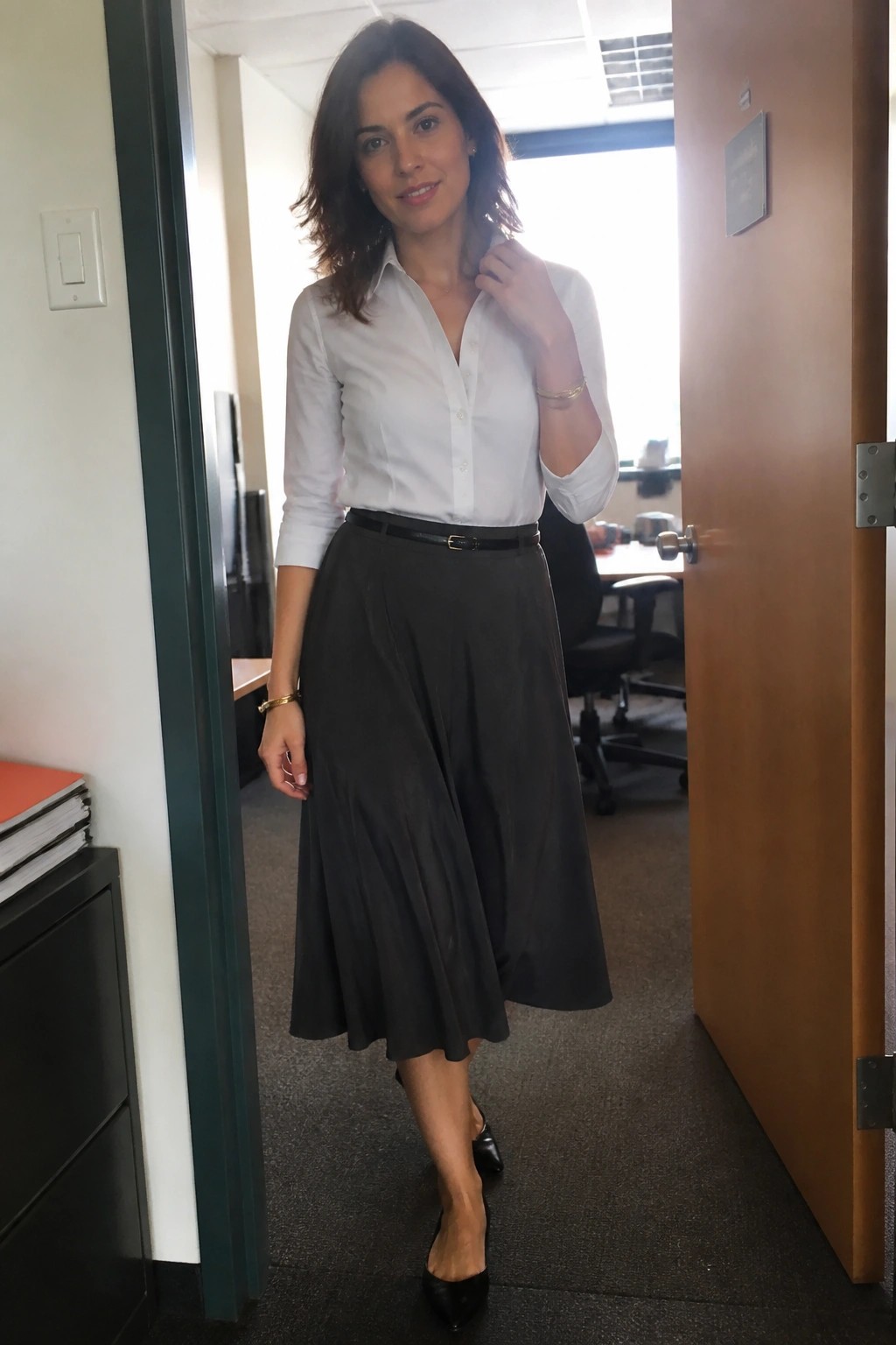 Woman in white shirt and gray pleated skirt standing in office doorway