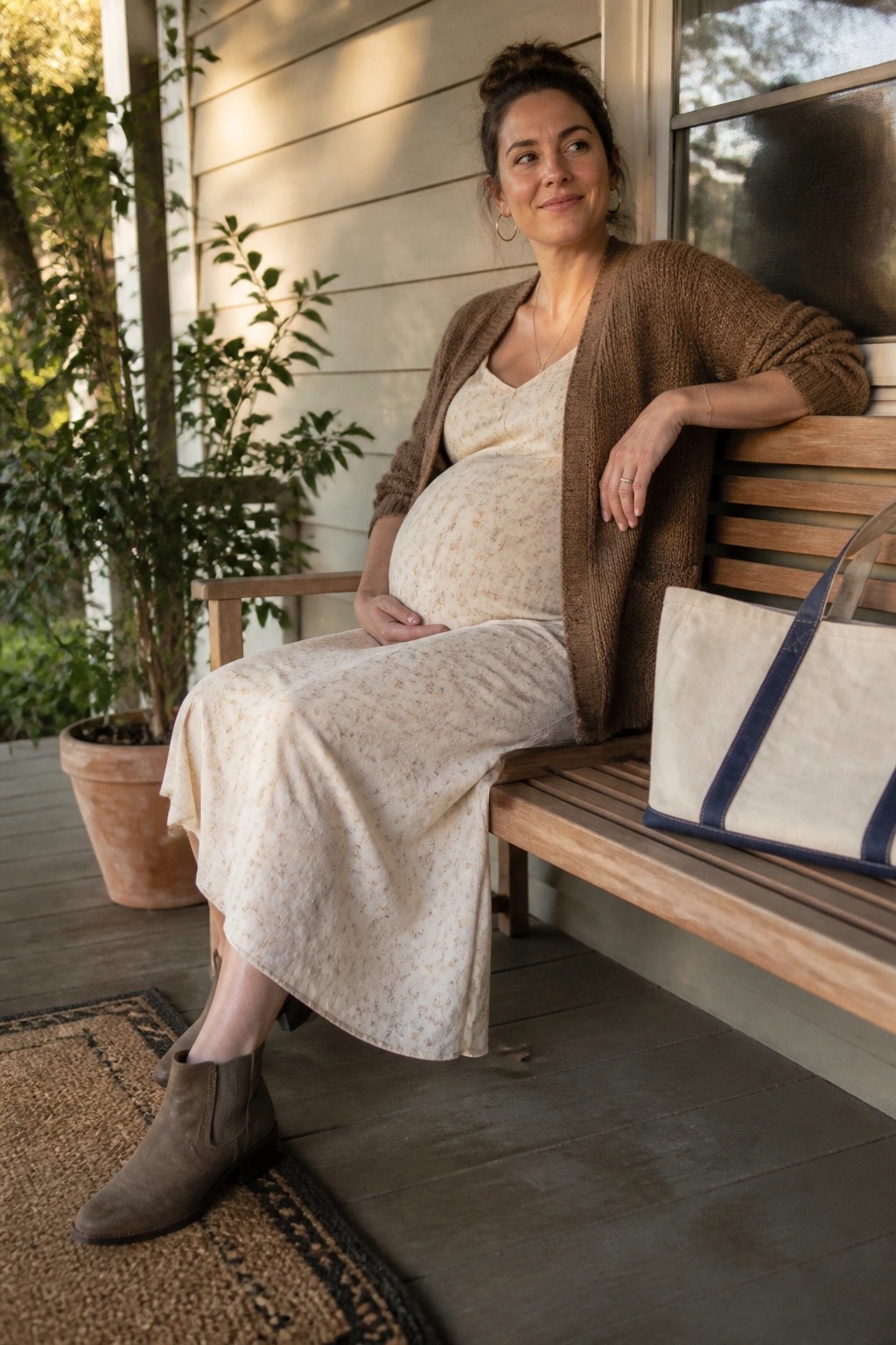 Pregnant woman in floral dress and brown cardigan on porch bench with tote bag