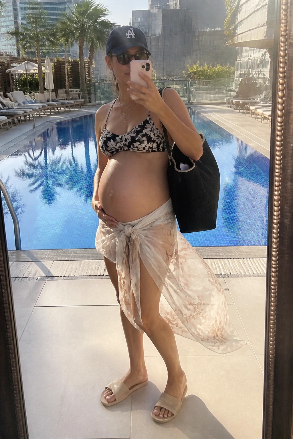 Pregnant woman in floral bikini and sarong taking selfie by rooftop pool