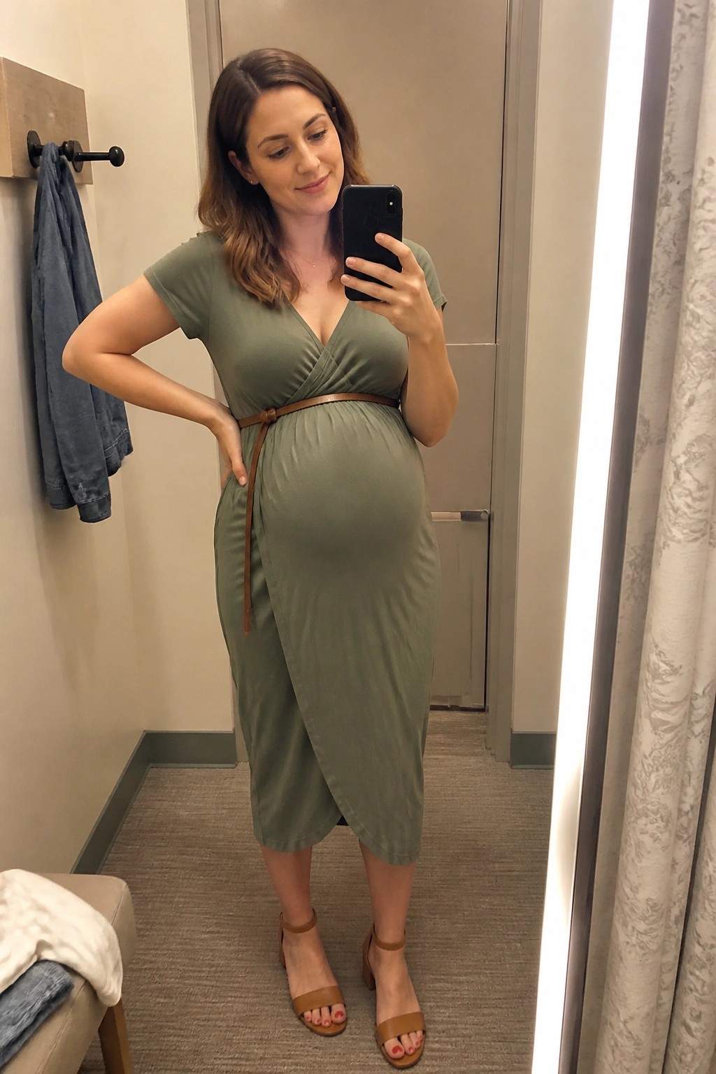 Pregnant woman in olive green dress taking mirror selfie with smartphone