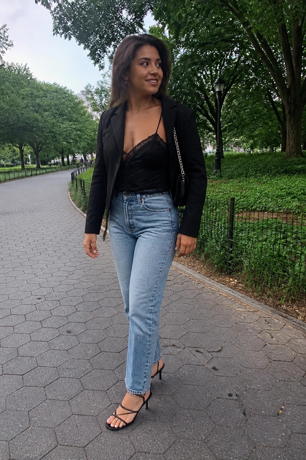 Woman in black blazer and jeans on park path with chain-strap bag