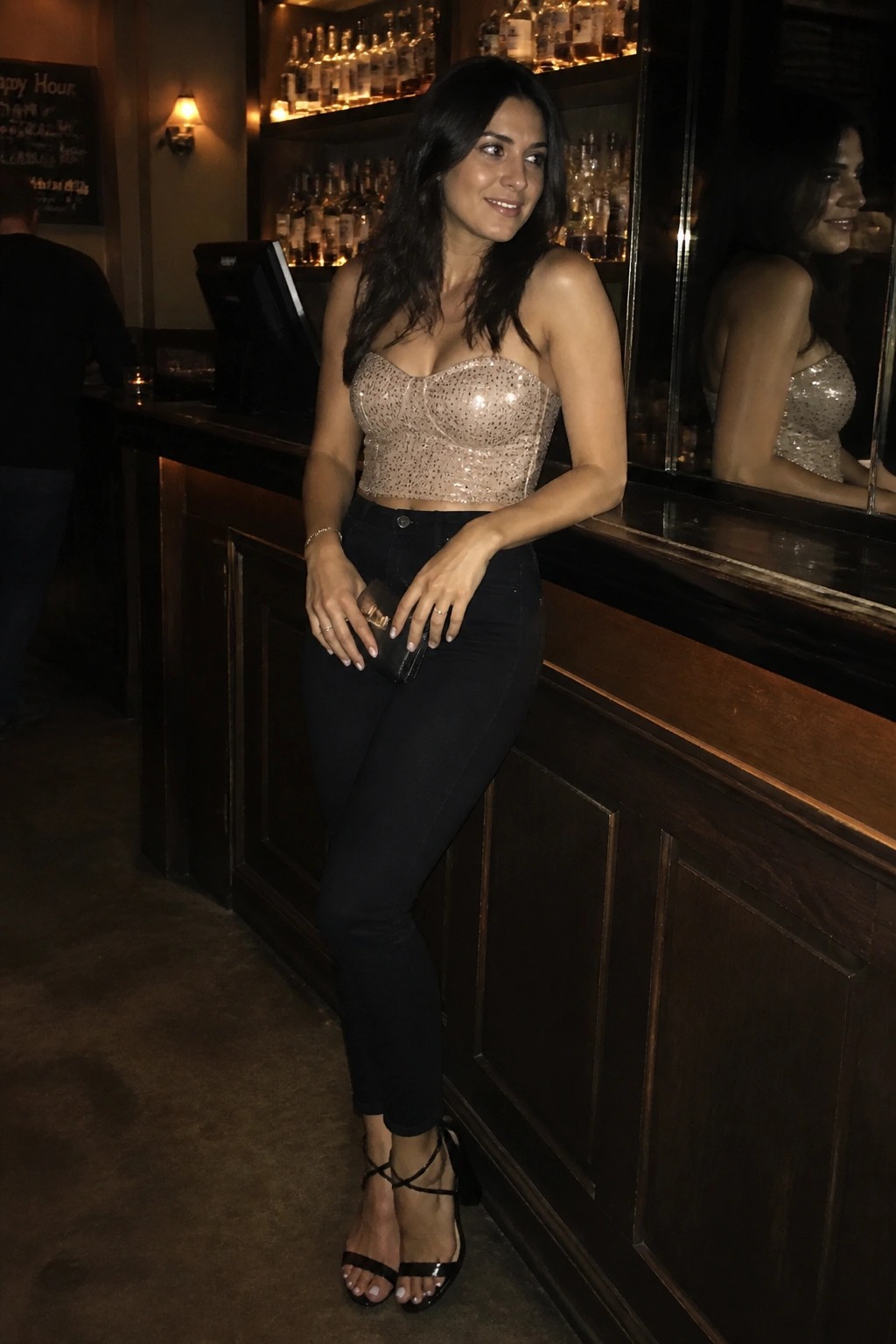 Woman in sequined crop top and black jeans leaning at bar counter