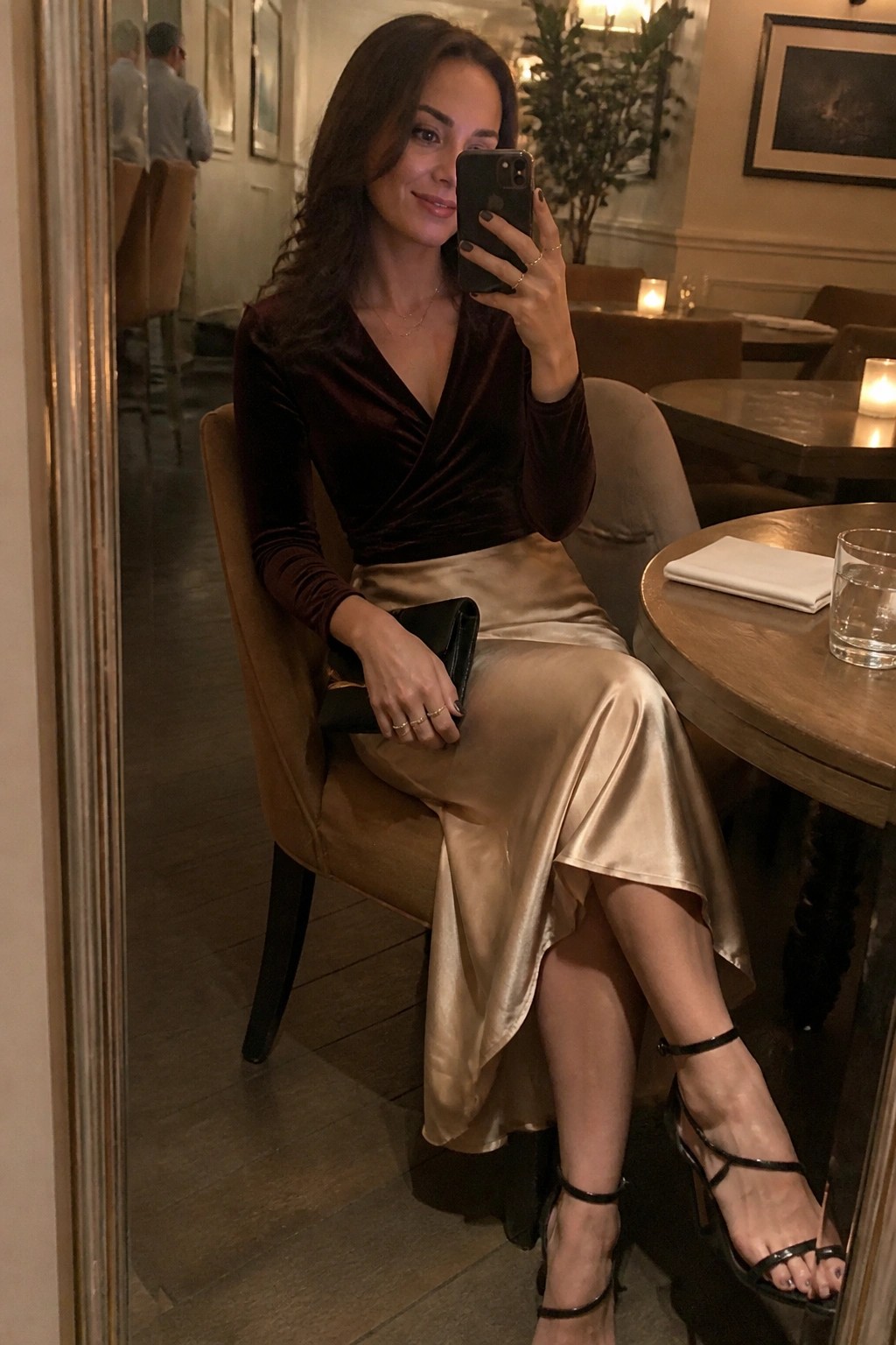 Woman in burgundy velvet top and gold satin skirt taking mirror selfie in restaurant