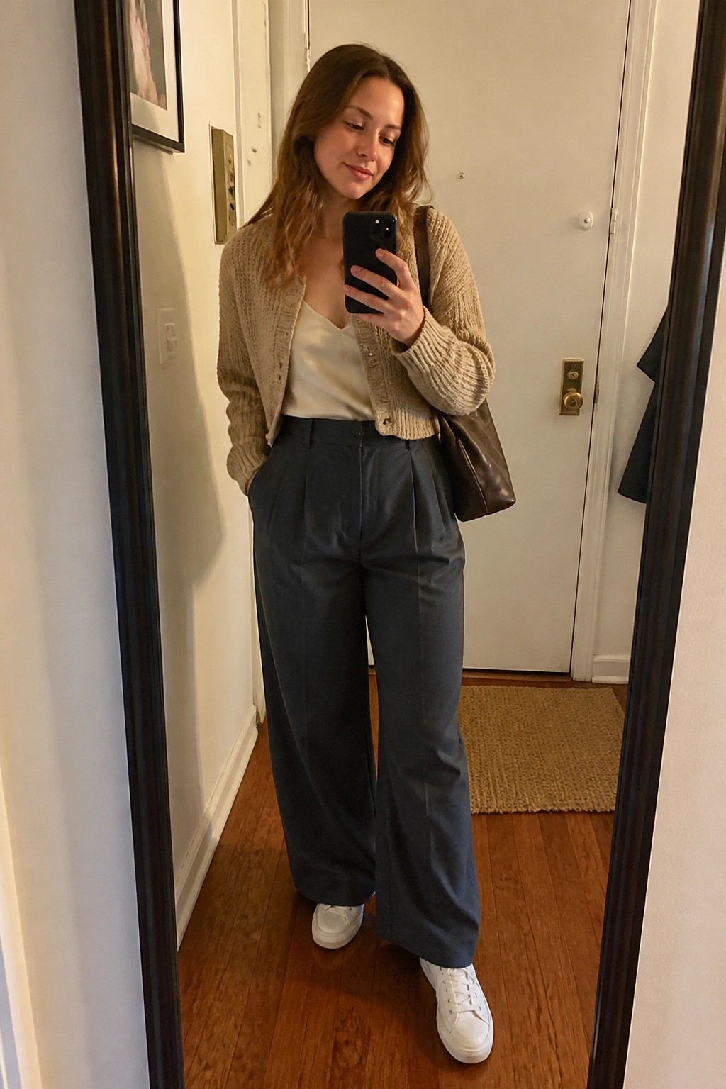Woman in beige cardigan and wide-leg pants taking mirror selfie with phone