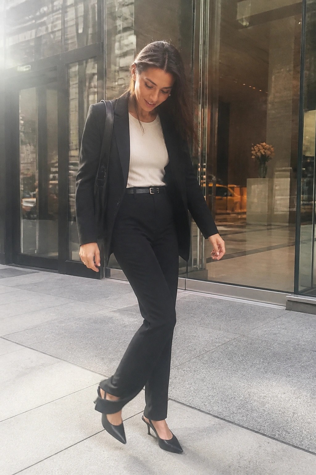 Woman in black pantsuit and white top walking by glass building doors