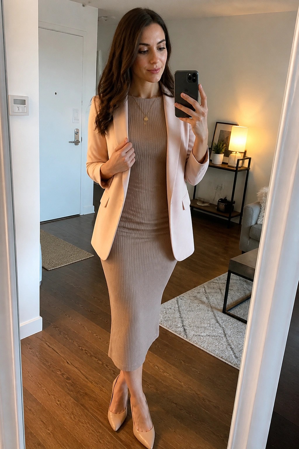 Woman in light pink blazer and beige ribbed dress taking mirror selfie