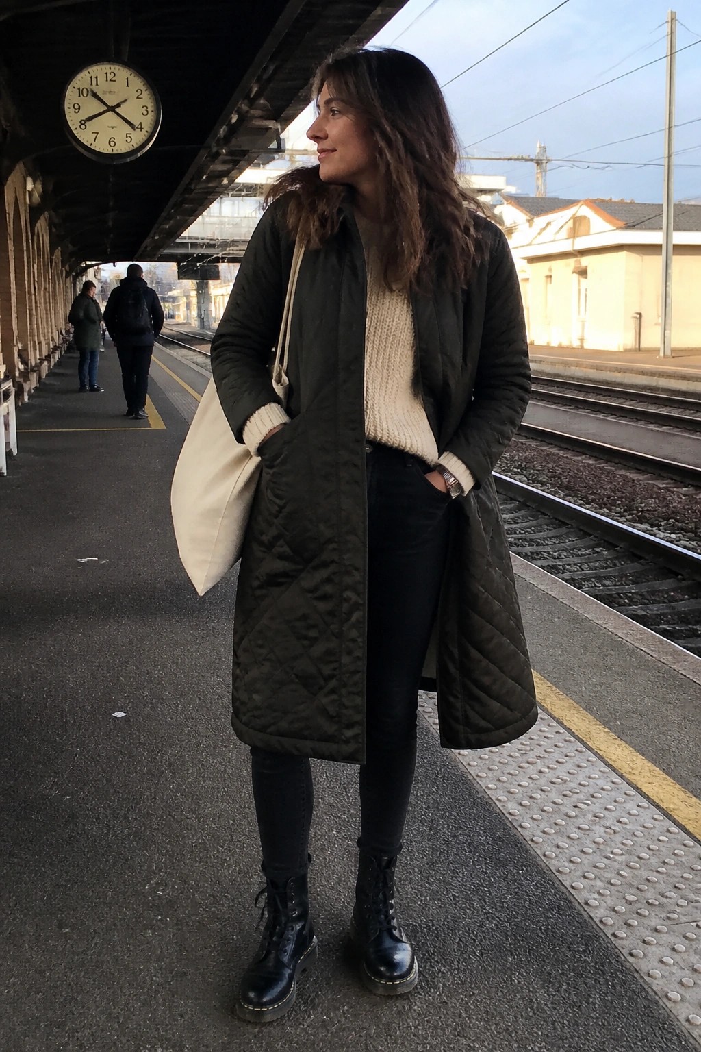 Woman in green quilted coat with tote bag on train platform