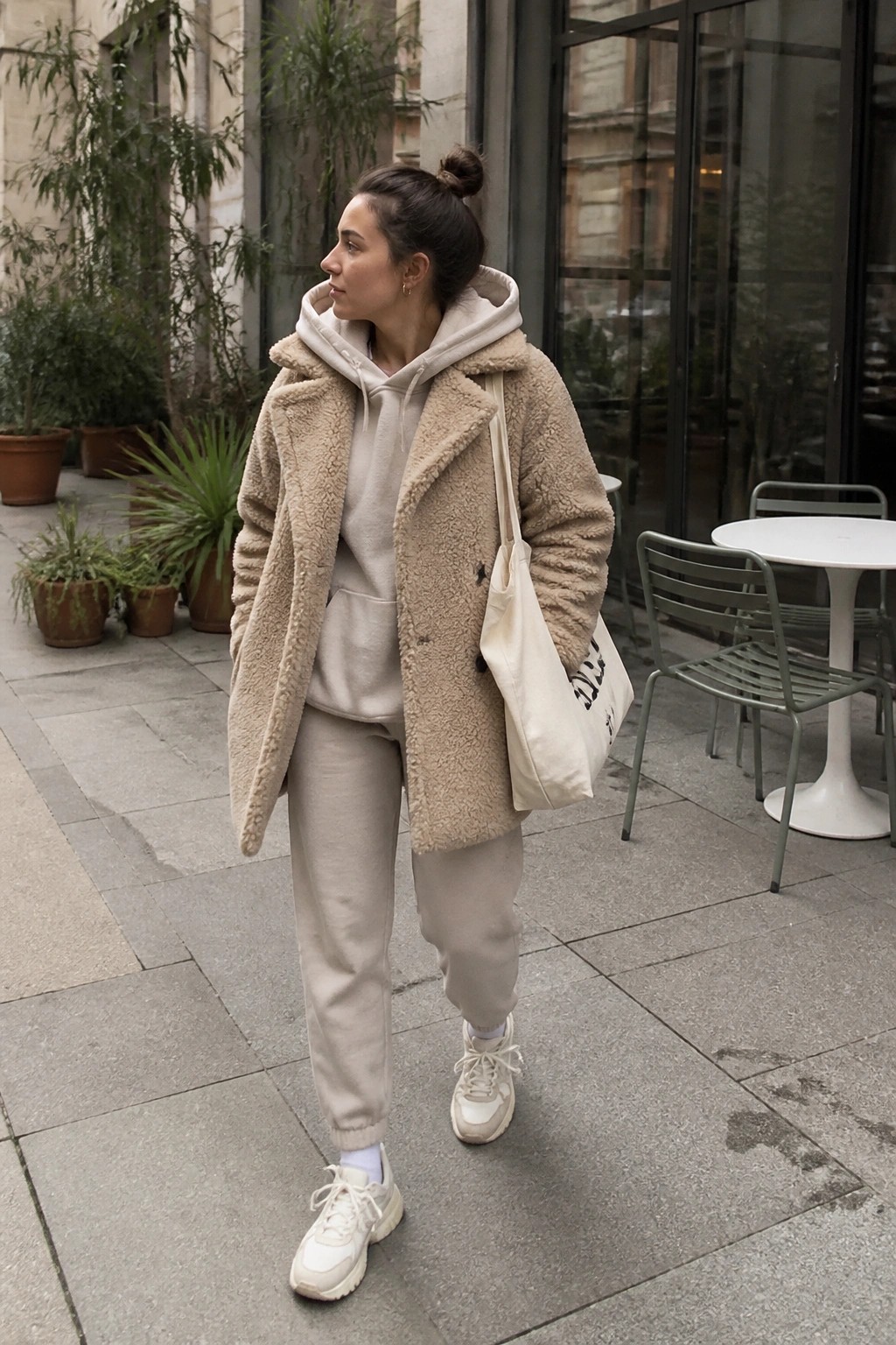 Woman in beige sherpa coat over sweatsuit with tote bag outdoors