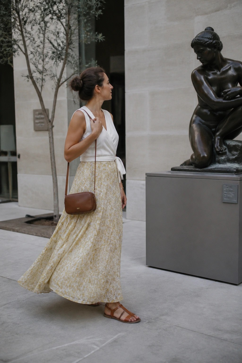 Woman in white top and yellow floral skirt beside bronze statue outdoors