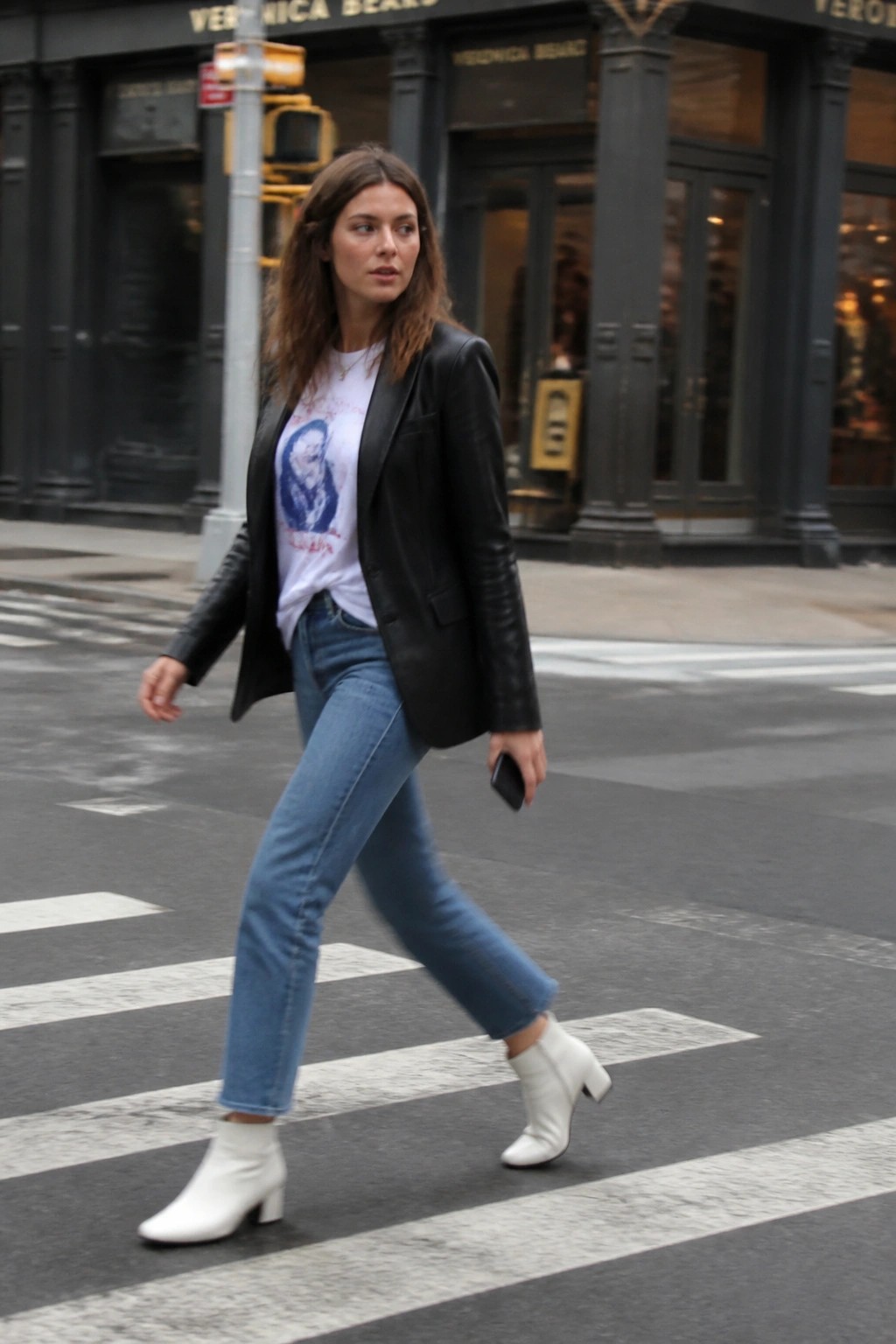 Woman in black leather jacket, jeans, and white boots crossing city street