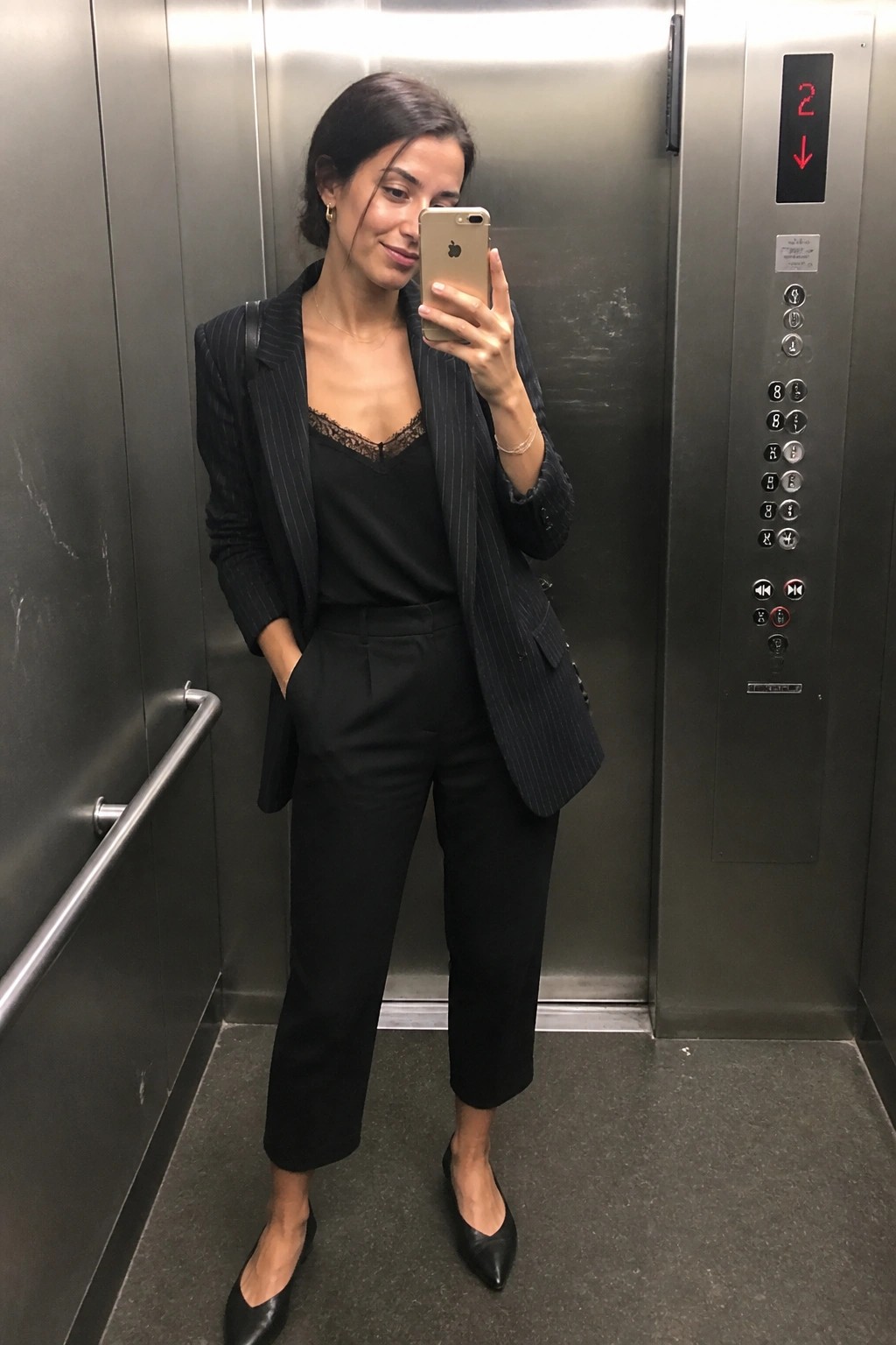 Woman in black pinstripe suit taking selfie in elevator with gold iPhone