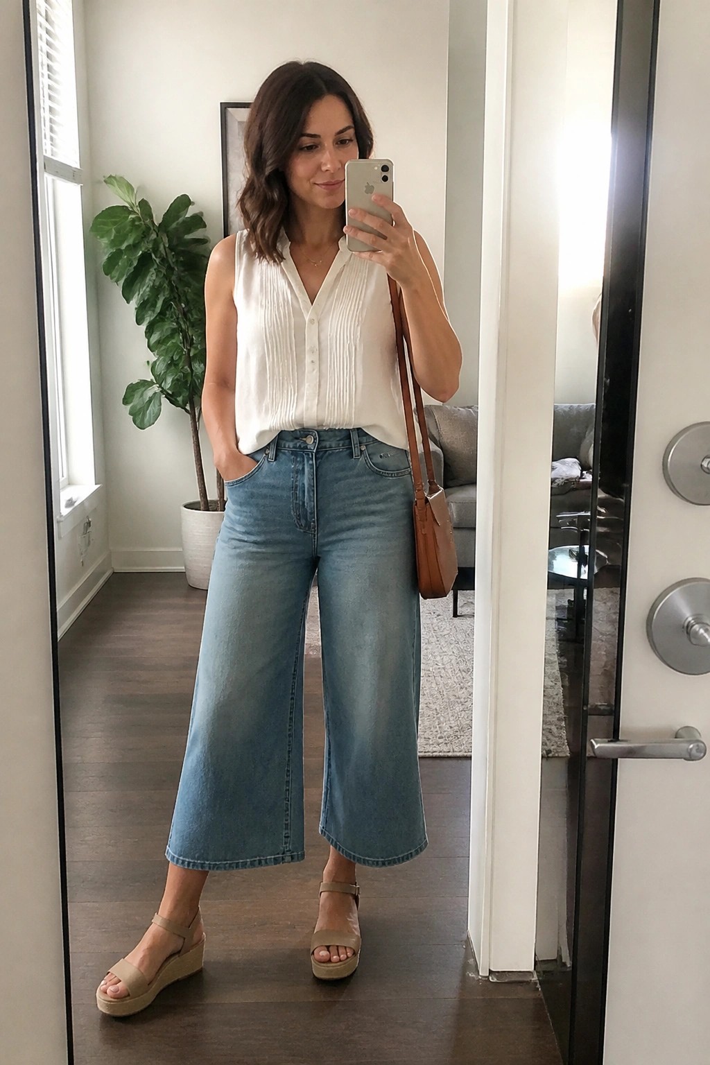 Woman in white sleeveless blouse and blue wide-leg jeans taking mirror selfie