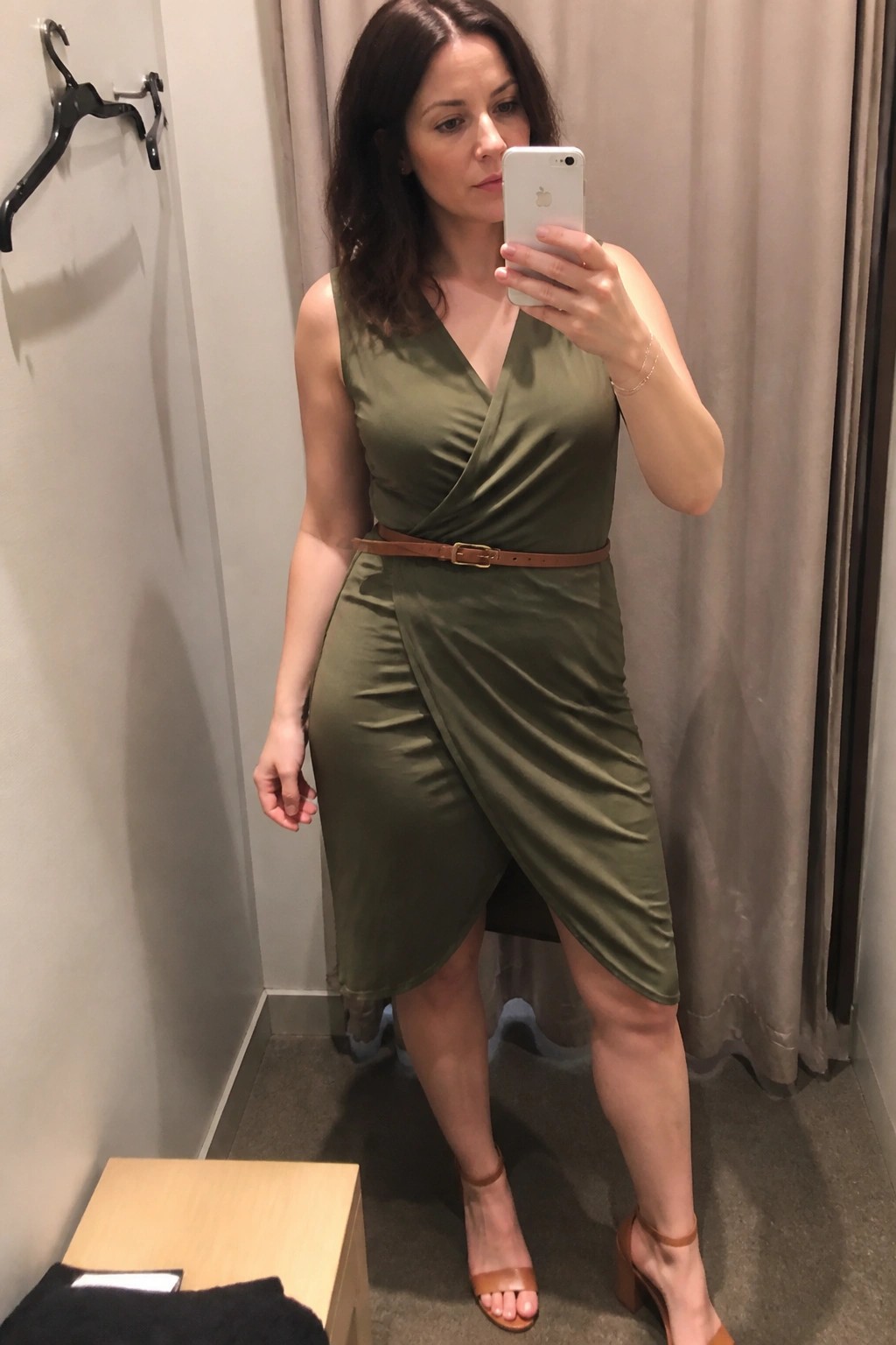 Woman in olive green wrap dress taking mirror selfie in fitting room