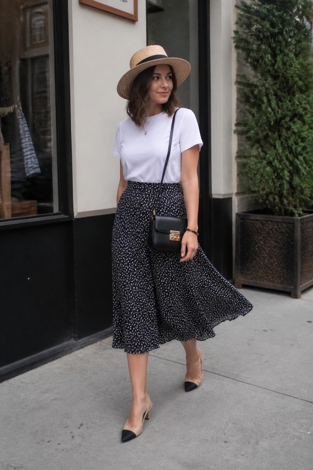 Woman in white tee, polka-dot skirt, straw hat, and pointed heels on sidewalk