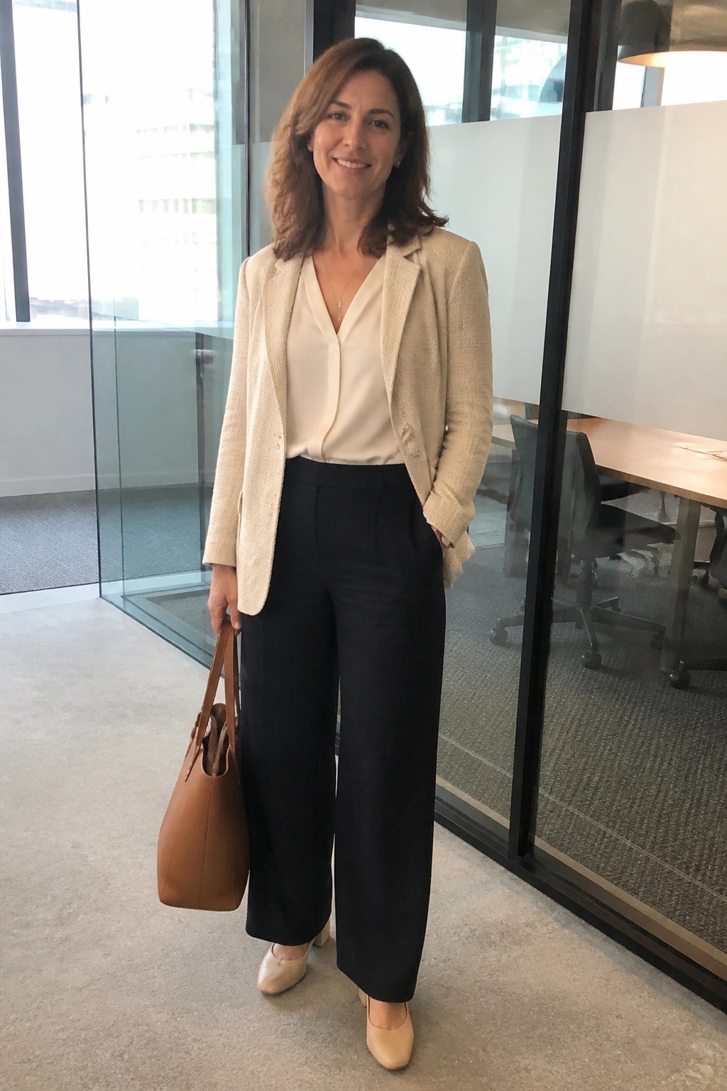 Woman in cream blazer and navy trousers holding tan handbag in office
