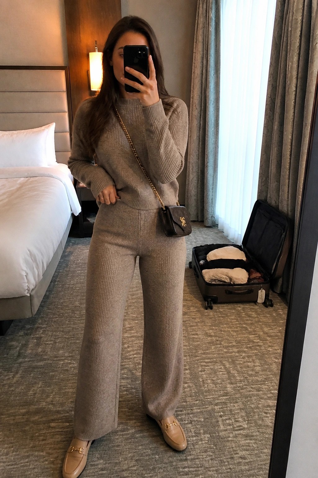 Woman in beige ribbed knit sweater set taking mirror selfie in hotel room