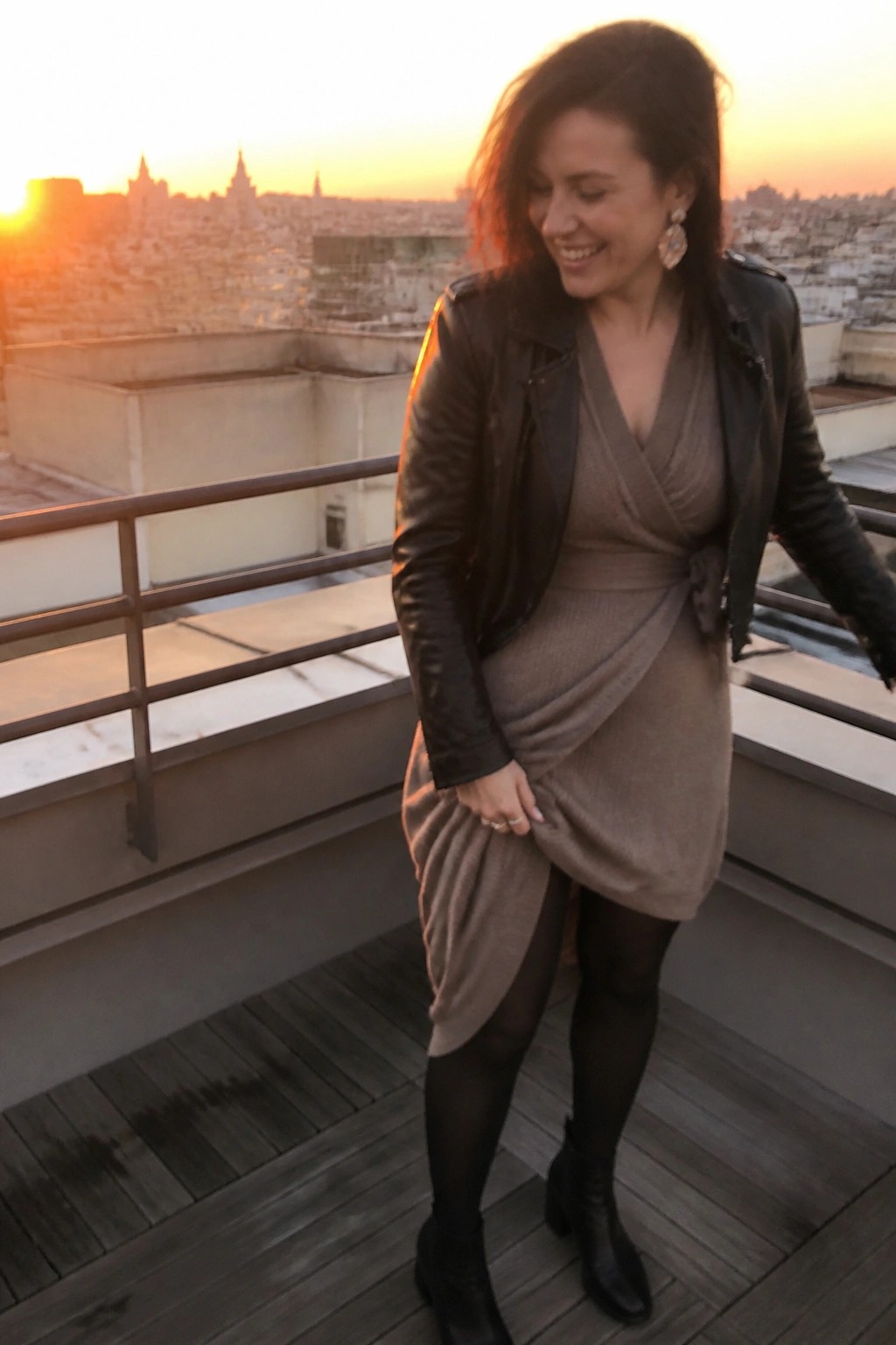 Woman in leather jacket and wrap dress on sunset city rooftop