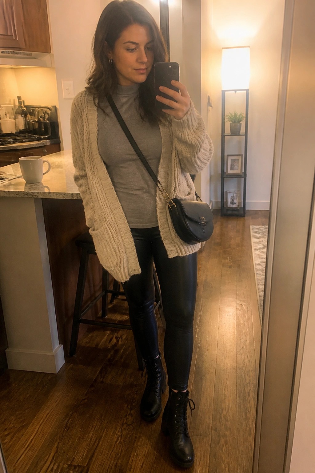 Woman in cream cardigan and leather leggings taking kitchen mirror selfie