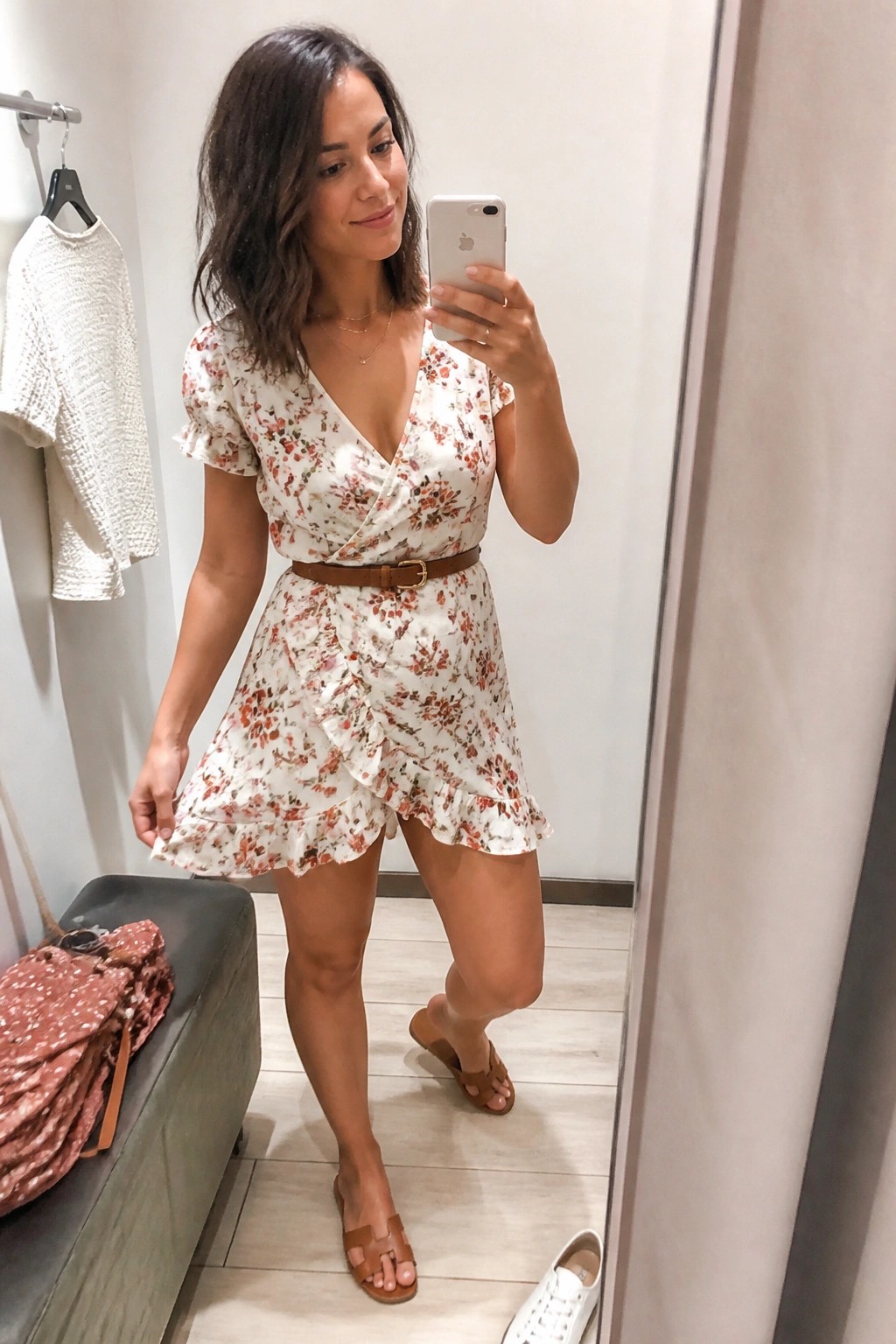 Woman in floral wrap dress with brown belt taking mirror selfie in fitting room