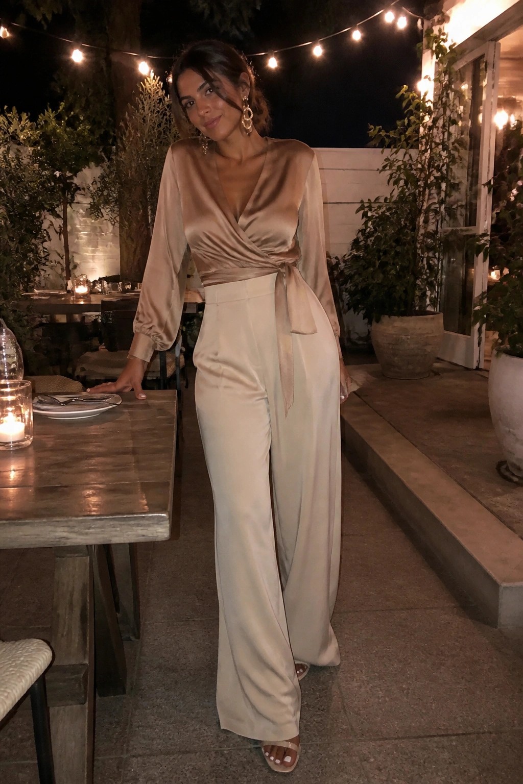 Woman in beige satin wrap top and wide-leg pants at outdoor night table