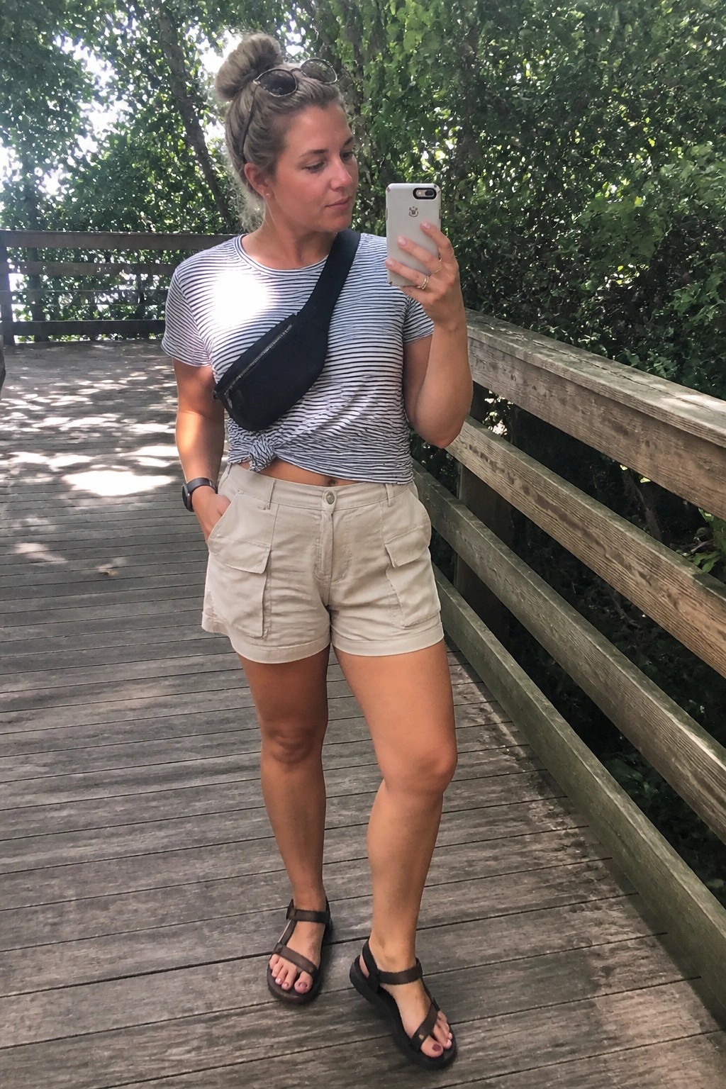 Woman in striped shirt and beige shorts taking selfie on wooden boardwalk