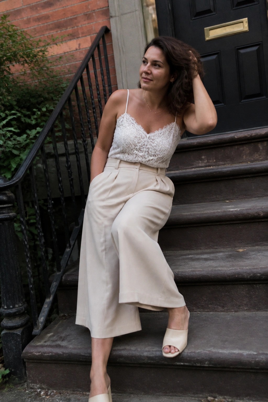 Woman in lace camisole and beige trousers seated on stone steps