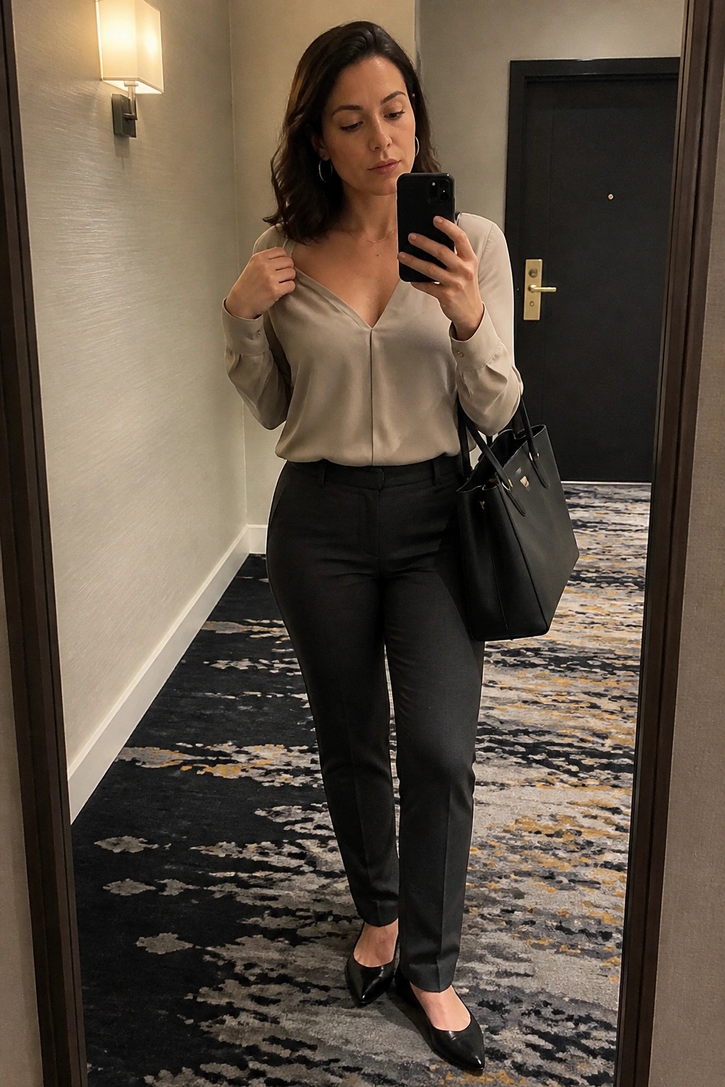 Woman in beige blouse and black pants taking mirror selfie with handbag