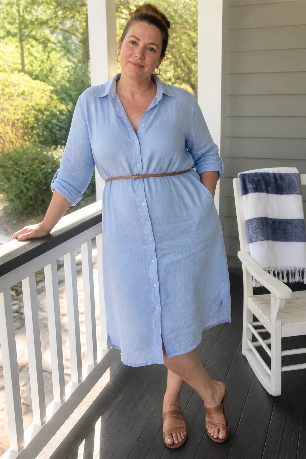 Woman in light blue button-down dress leaning on porch railing by rocking chair