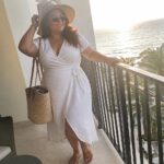 Woman in white wrap dress and straw hat on sunny ocean balcony