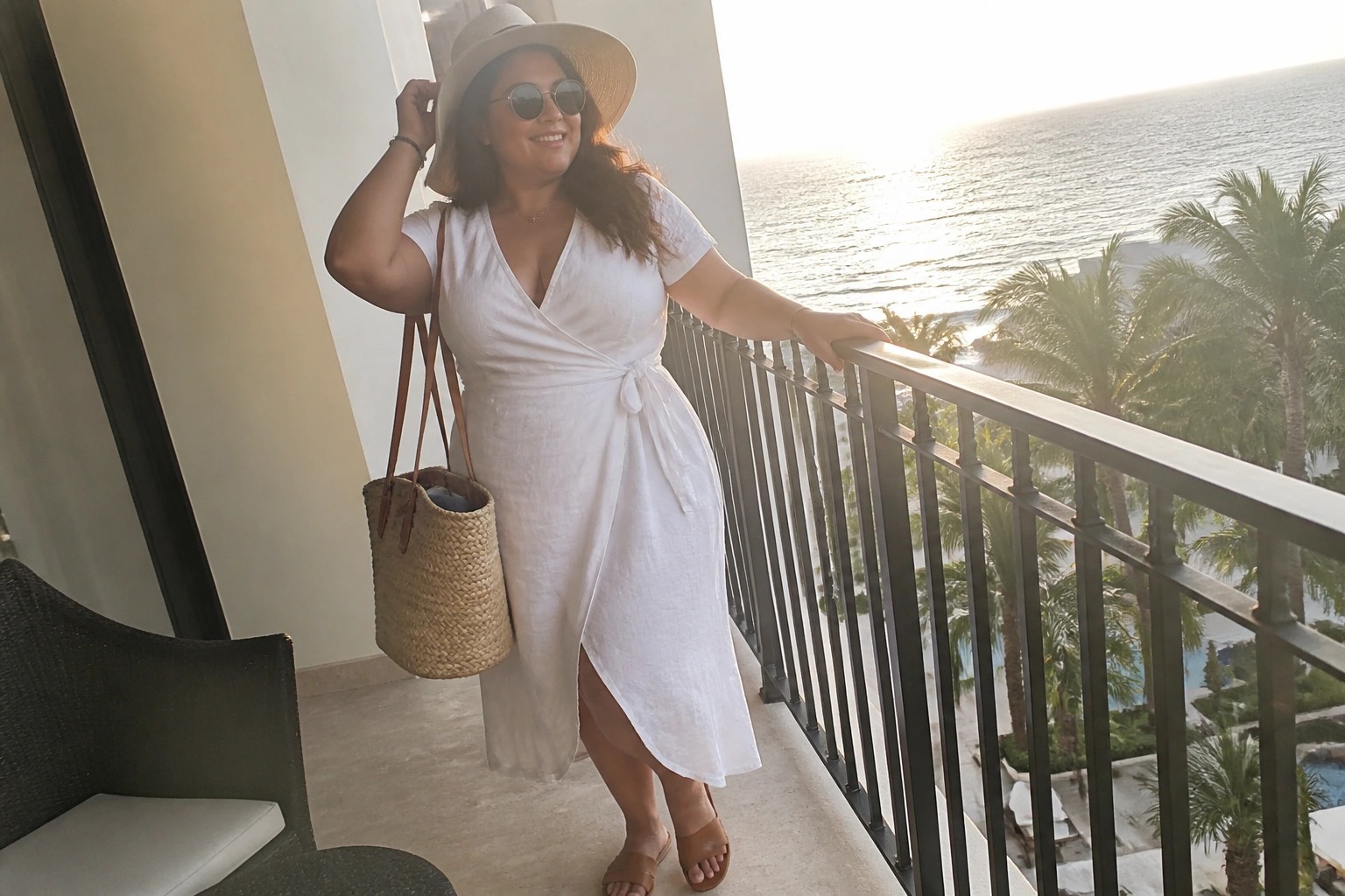 Woman in white wrap dress and straw hat on sunny ocean balcony