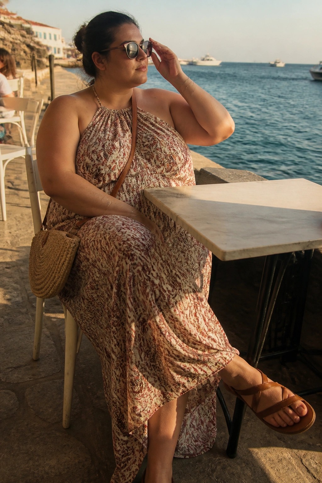 Plus size woman wearing a floral print halter maxi dress with brown cross strap sandals and a round woven straw bag.