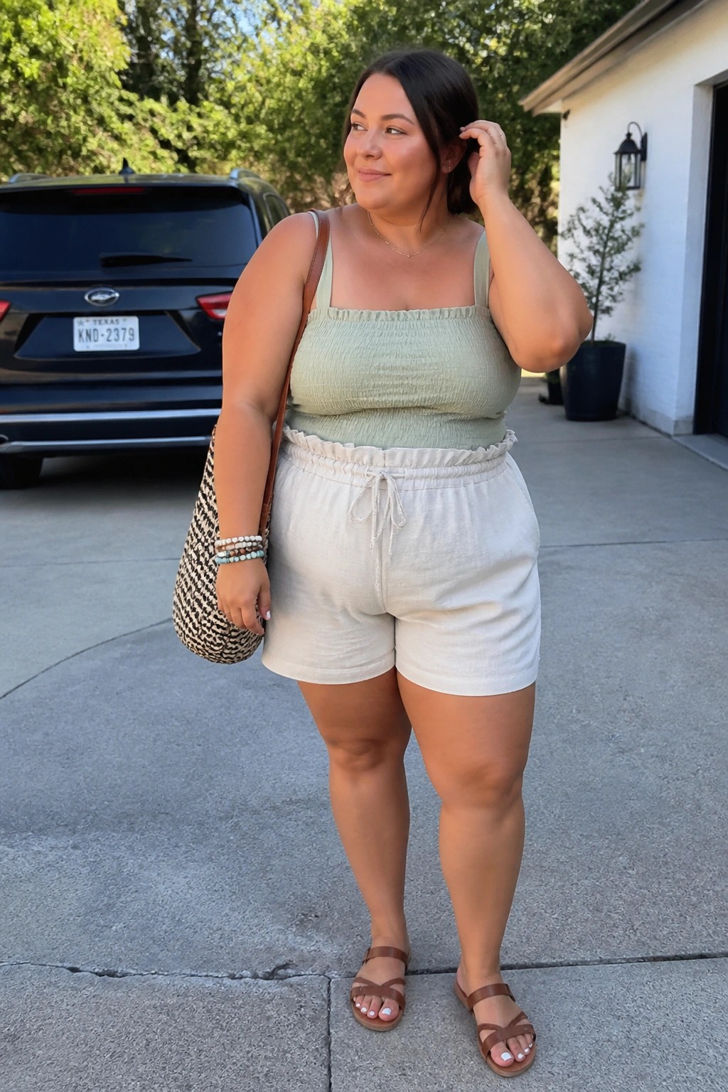 Woman in sage green smocked top and white linen shorts holding woven bag