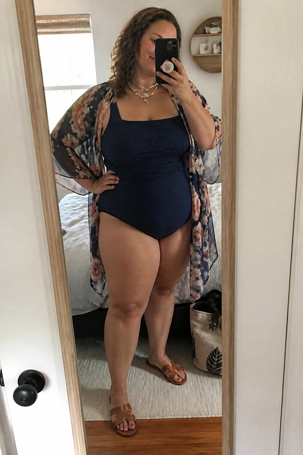 Curvy woman in navy swimsuit and floral kimono taking bedroom mirror selfie