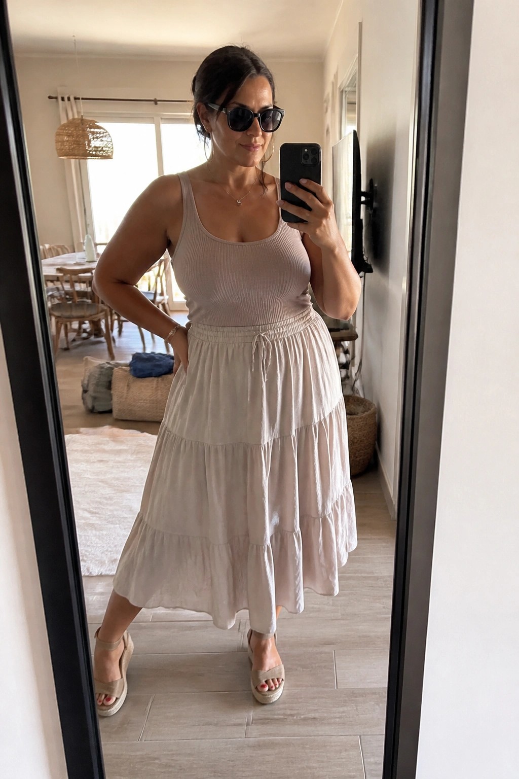 Woman in beige tank top and tiered skirt taking mirror selfie indoors