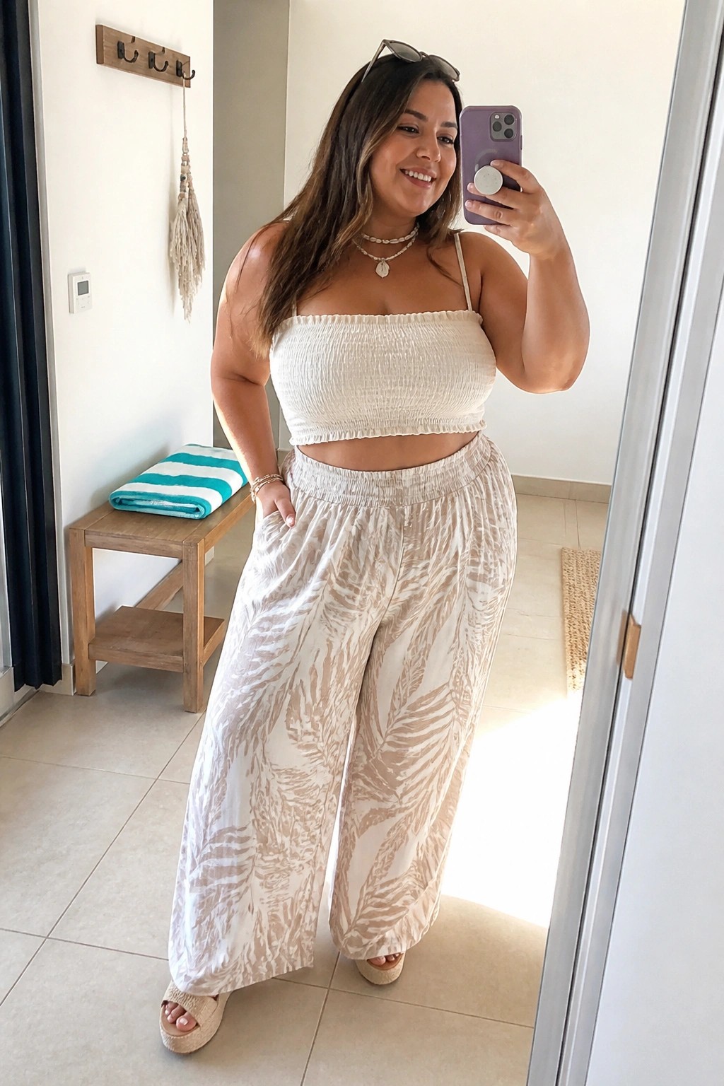 Plus size woman in cream smocked crop top and beige leaf print wide leg pants with platform sandals taking a mirror selfie.